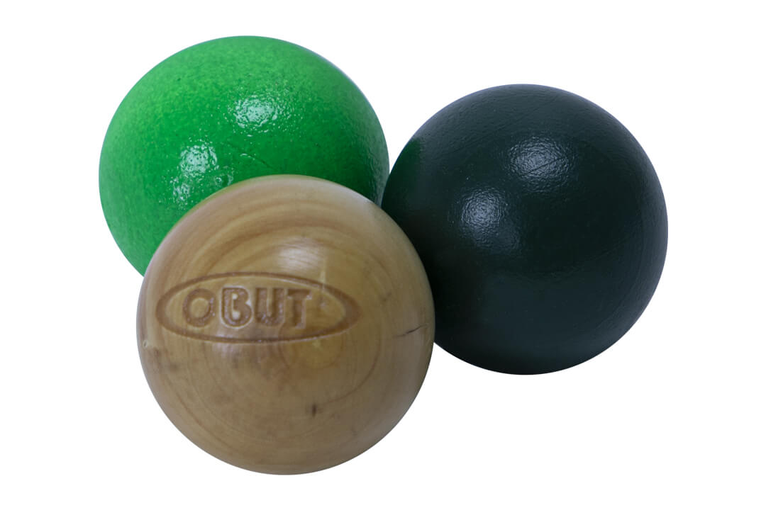 Three pétanque jacks, with two colored in vibrant green and deep black, and one natural boxwood jack with the brand 'OBUT' engraved. They are closely grouped together against a white background.